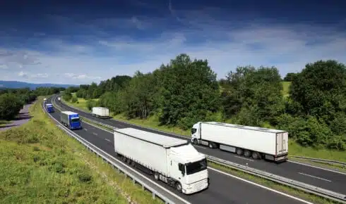 Klimatregler inom transport: Flera lastbilar k&ouml;r p&aring; en flerfilig motorv&auml;g genom gr&ouml;nt kuperat landskap &ndash; en bild p&aring; den v&auml;gtransport som omfattas av EU:s klimat- och utsl&auml;ppsregler